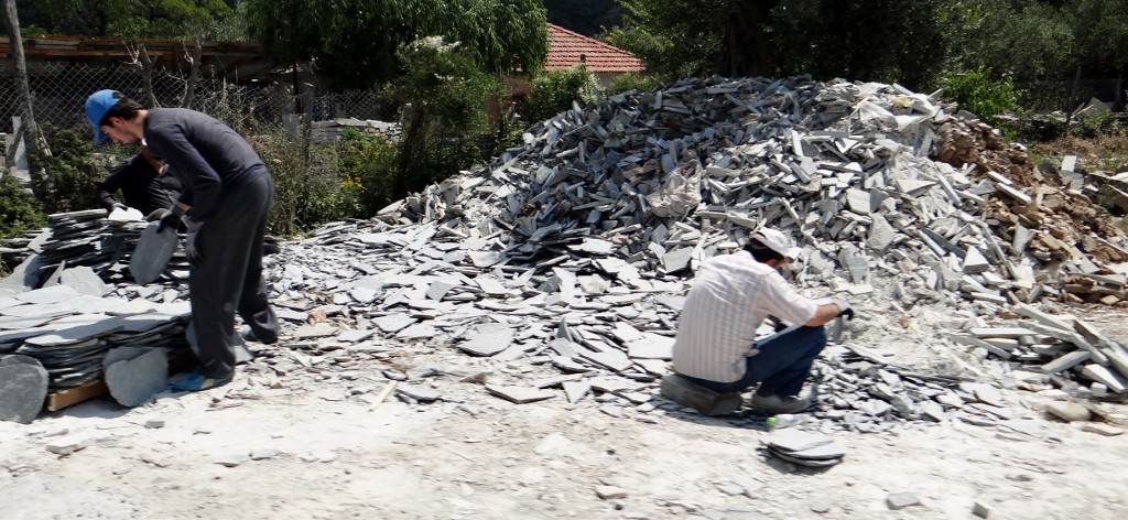 Three men at the roadside chipping away at a pile of slate offcuts to make some tiles.