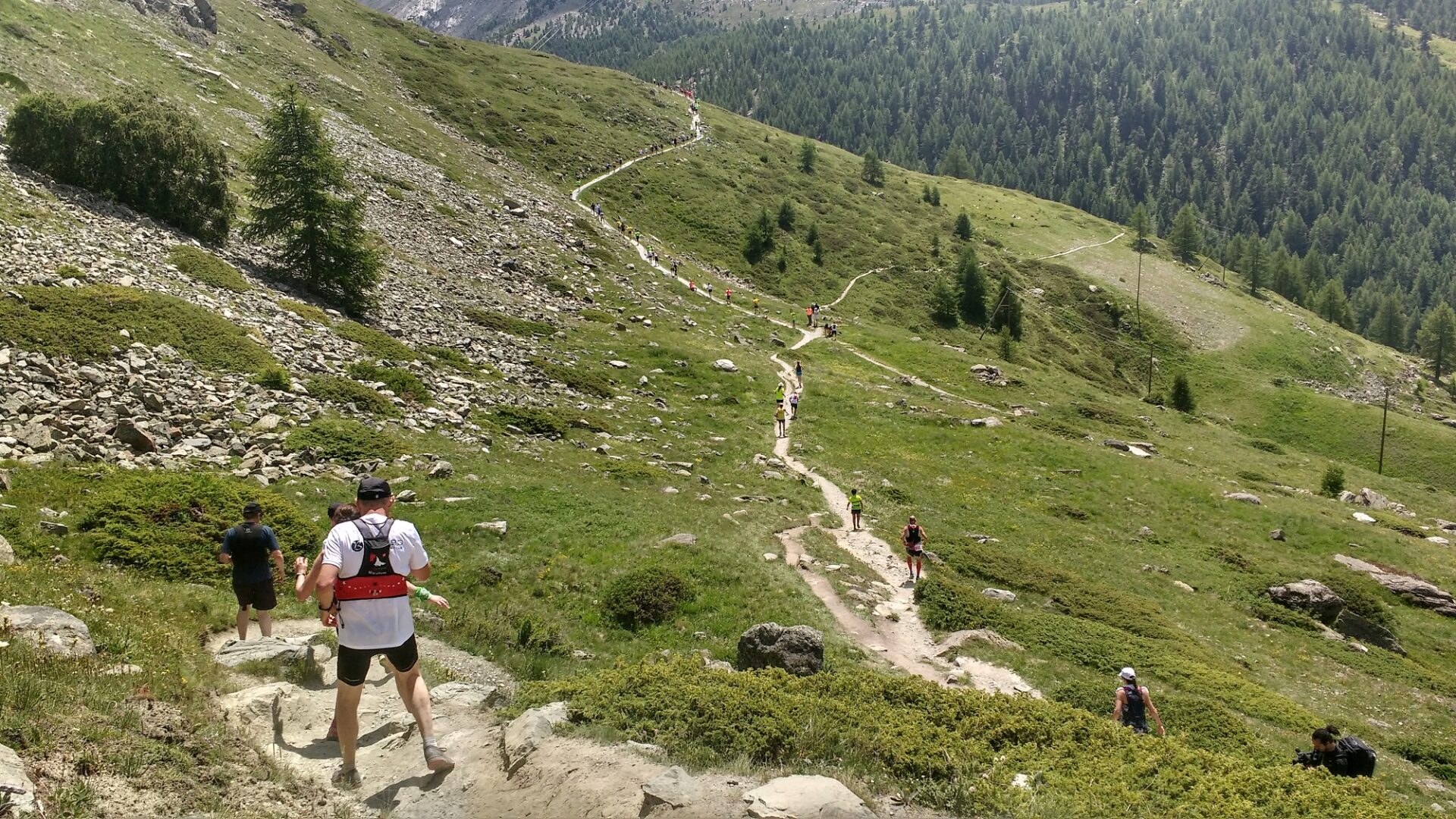 Runners in the sun, crossing the side of a valley on the Zermatt Marathon
