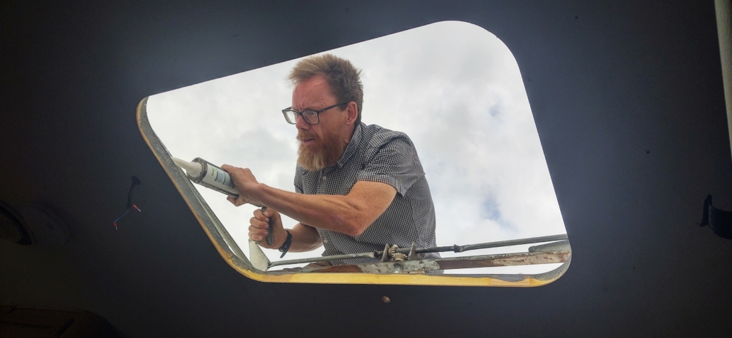 Man squeezing mastic sealant onto a motorhome roof.