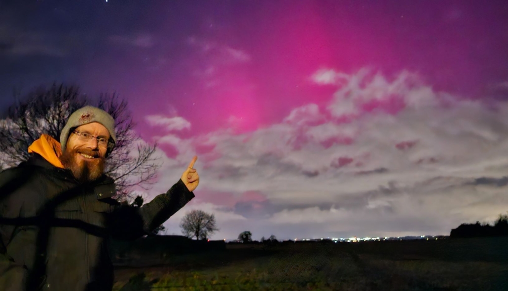 Jason in front of a sky lit pink by the northern lights