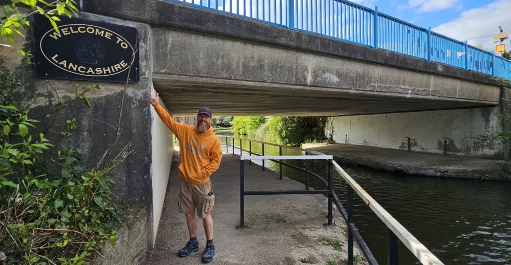 Jay stood by canal bridge with Welcome to Lancashire sign 