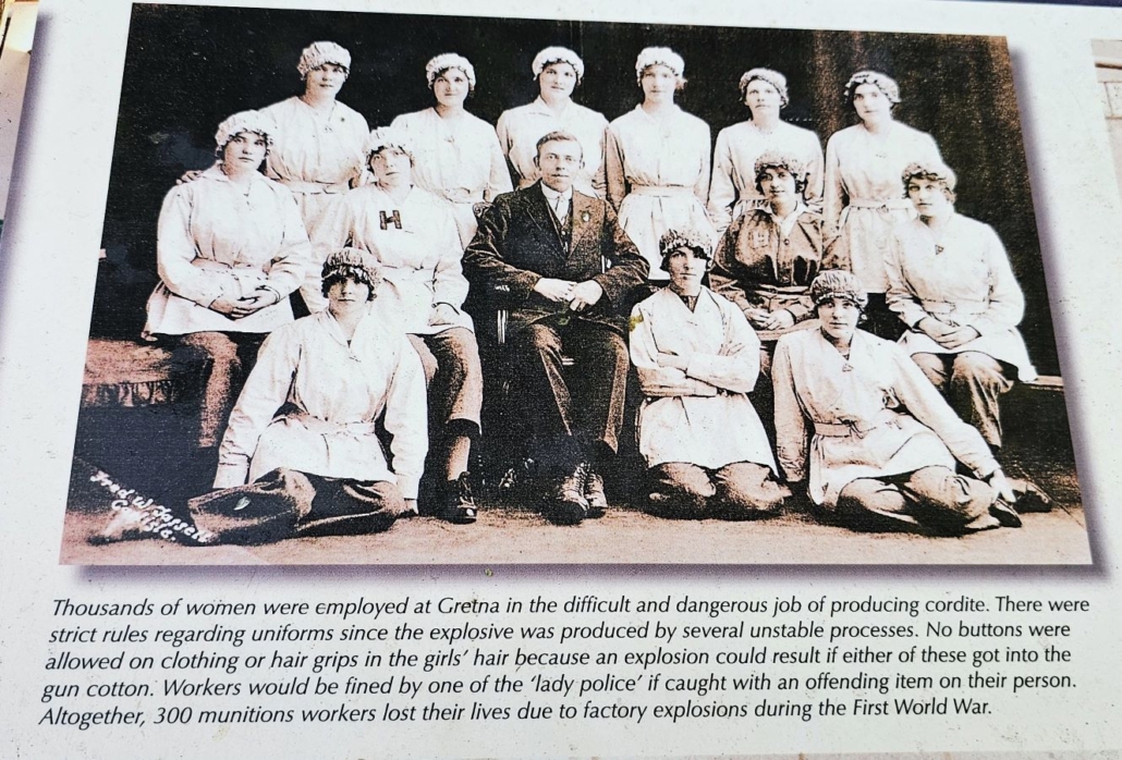 Information board with photo of 'Gretna Girls' in the uniforms they had to wear to reduce the chance of an explosion while working with the cordite.