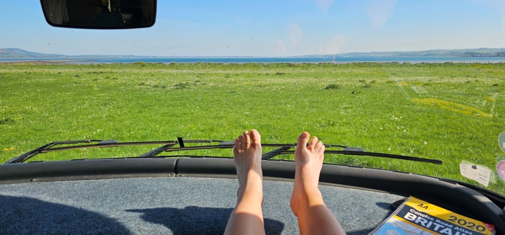 Feet on a motorhome dashboard in the sun looking out across Loch Ryan.