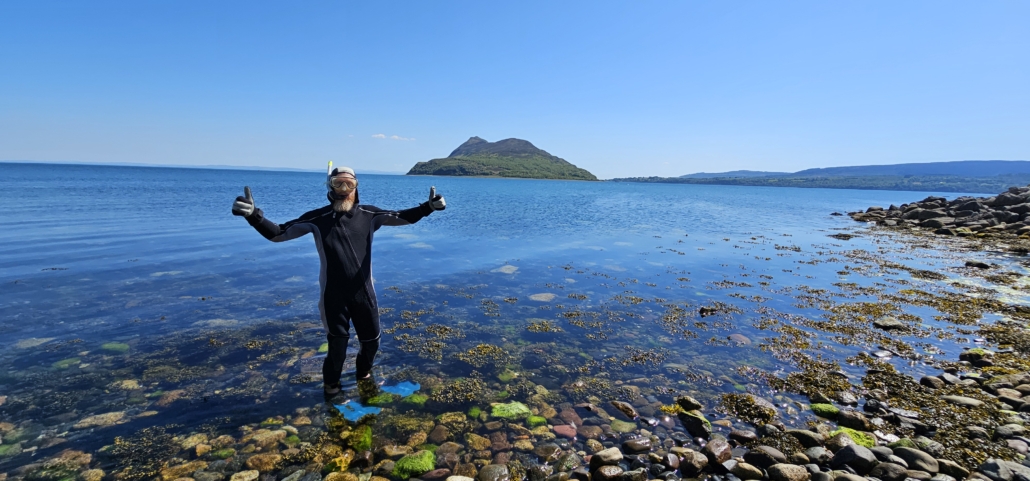 Jay in wetsuit setting off to snorkel in the seas with Holy Island in the background