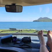 Feet on motorhome dashboard with view of sea and an island through the windscreen