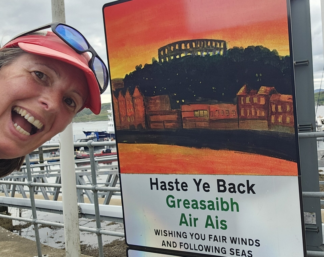 Ju in front of a sign in Oban saying Haste ye back