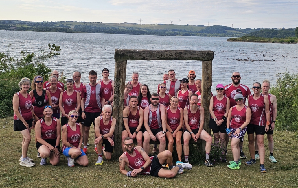 Running club members posing for a group photo by a lake