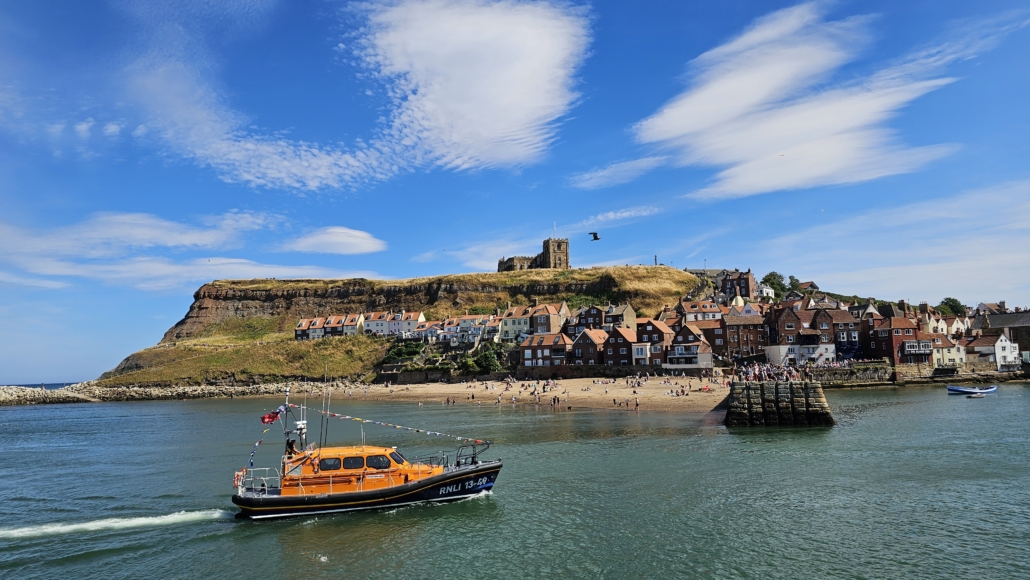 Blue skies, Whitby Abbey ruins on the headland and a lifeboat in the sea in the foreground