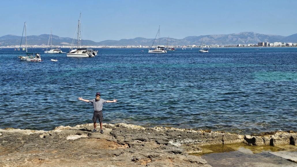 Jay stood on rocks by a sea with boats in the background